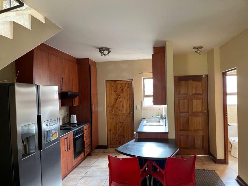 A functional kitchen featuring wooden cabinetry, built-in oven and hob, tiled flooring, and direct access to adjacent rooms and a staircase.