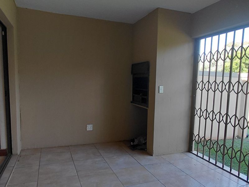 A covered patio area featuring tiled flooring, a built-in braai, and secure sliding door access to the garden.