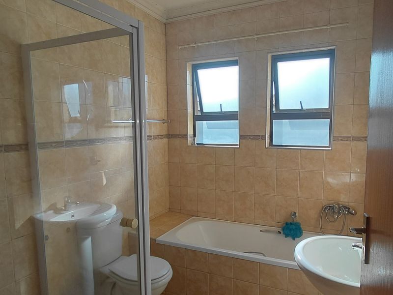 A functional bathroom featuring a built-in bathtub, separate shower enclosure, pedestal basin, and toilet with neutral wall tiling.