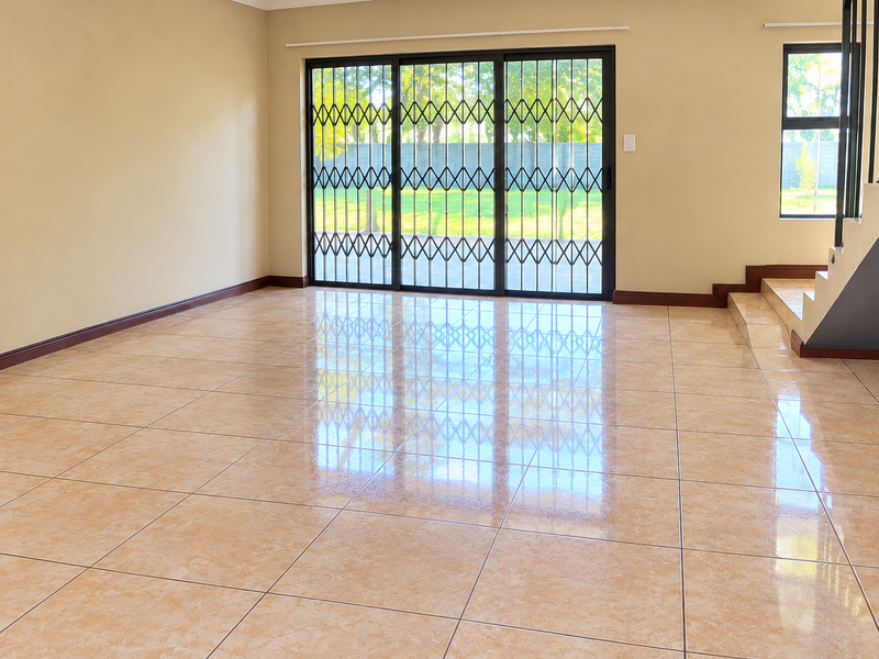 A spacious, empty living area featuring polished ceramic tile flooring, a staircase, and large sliding glass doors with security gates leading to the garden.