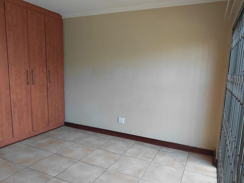 An empty bedroom featuring tiled flooring, built-in wooden cupboards, and a security gate over the window.