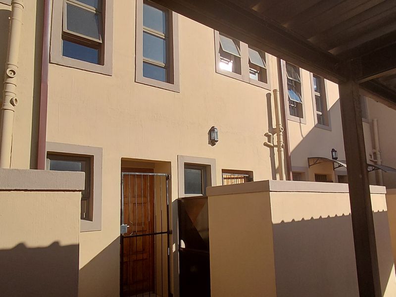 Front exterior view of a townhouse featuring a covered carport, paved driveway, and secure entrance with a security gate.