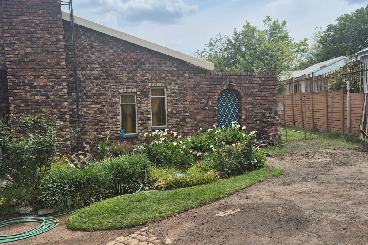 Rear exterior view of a face brick house featuring a garden bed, lawn area, and an arched side gate.