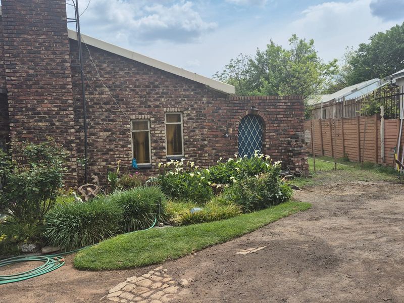 Rear exterior view of a face brick house featuring a garden bed, lawn area, and an arched side gate.