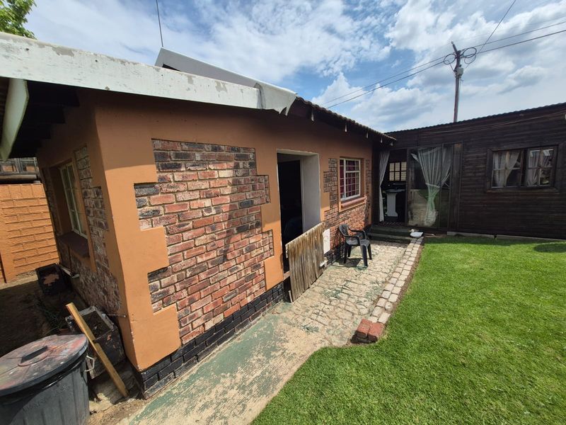 Rear view of the property featuring a brick and timber facade, paved walkway, and a small garden area.