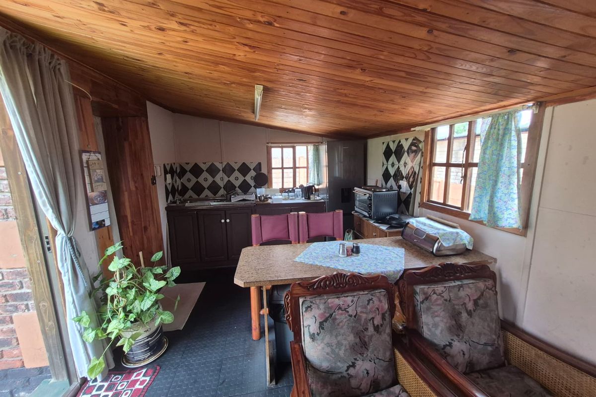 A compact kitchen area featuring timber ceiling paneling, built-in cabinetry, and a tiled backsplash, offering a functional space with potential for modernization.