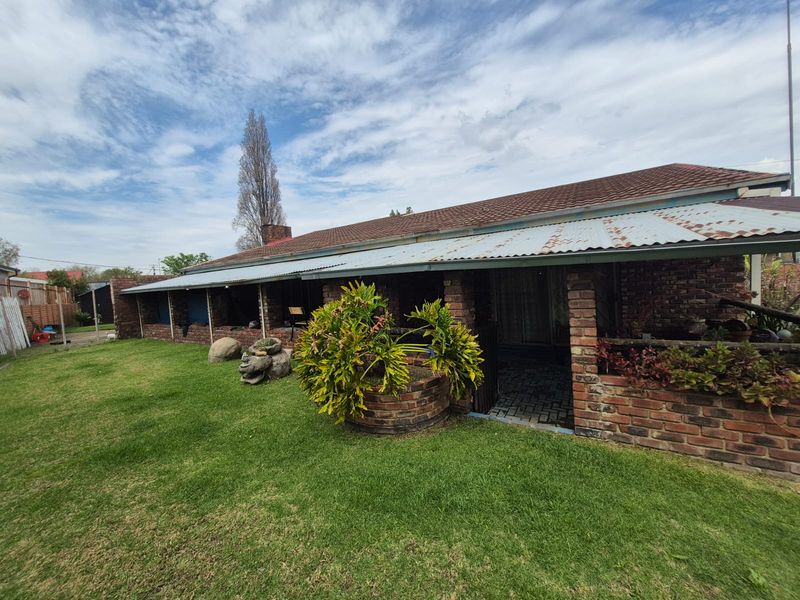 Rear view of a brick house featuring a covered patio area, a corrugated metal roof, and a surrounding garden space.