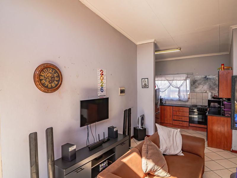 Open-plan living area featuring tiled flooring and a functional kitchen with built-in cabinetry, oven, and hob, offering a practical layout for daily living.