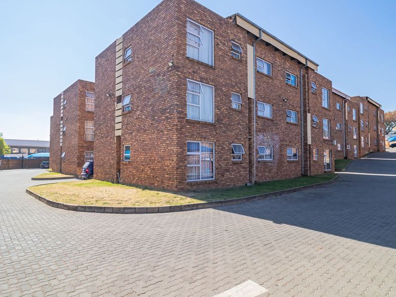 Exterior view of a multi-story face brick apartment complex featuring paved parking areas and covered parking bays.