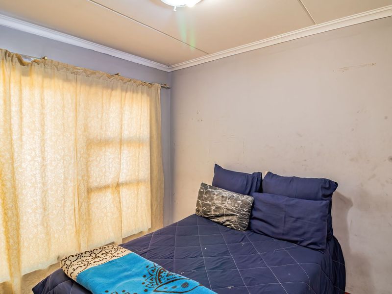 A bedroom featuring a ceiling light fixture and cornice, currently showing signs of wear on the wall surfaces.
