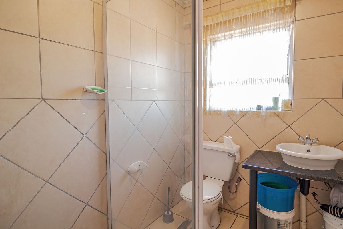 A functional bathroom featuring a shower enclosure, toilet, and a vanity basin with tiled walls and flooring.