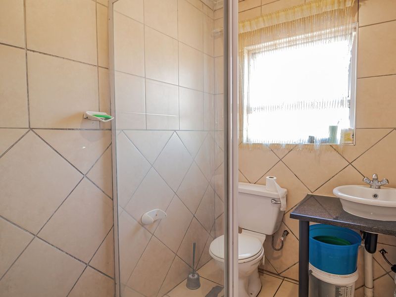 A functional bathroom featuring a shower enclosure, toilet, and a vanity basin with tiled walls and flooring.
