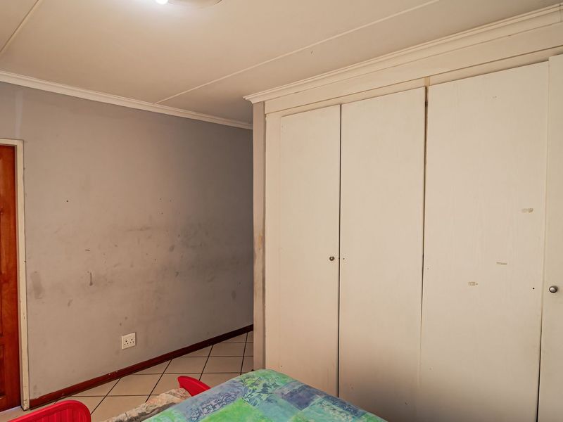 A bedroom featuring built-in cupboards, tiled flooring, and a wooden door. The walls show visible scuff marks and require maintenance.