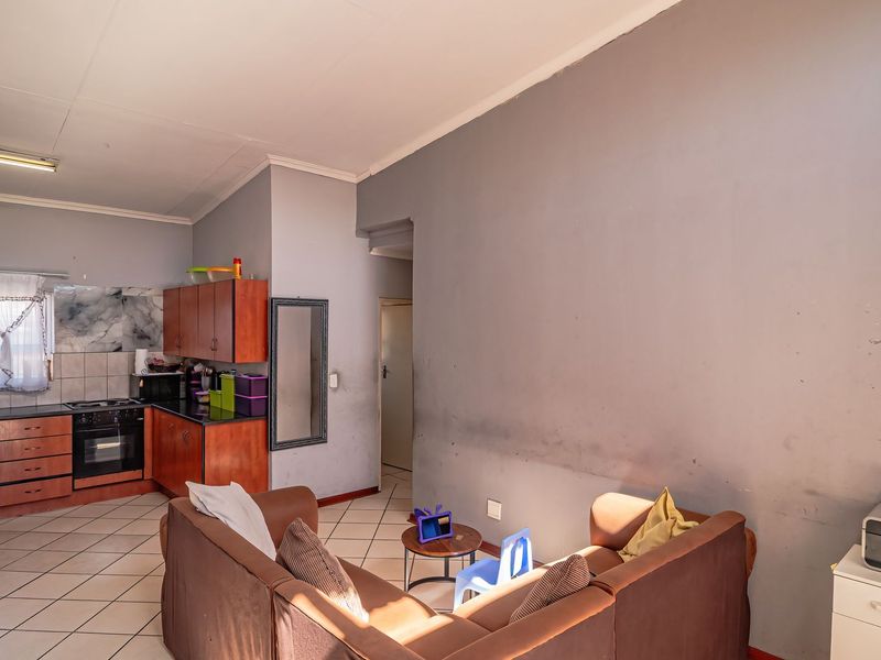 Open-plan living area featuring a compact kitchen with built-in cabinetry, oven, and hob, finished with tiled flooring throughout.