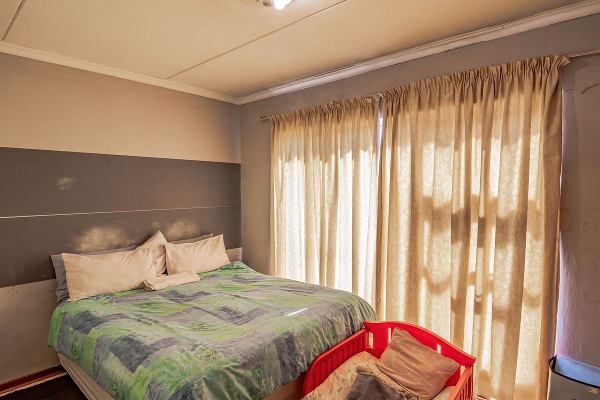 A bedroom featuring a sliding door with curtains and painted wall accents, showing signs of wear and surface damage requiring maintenance.