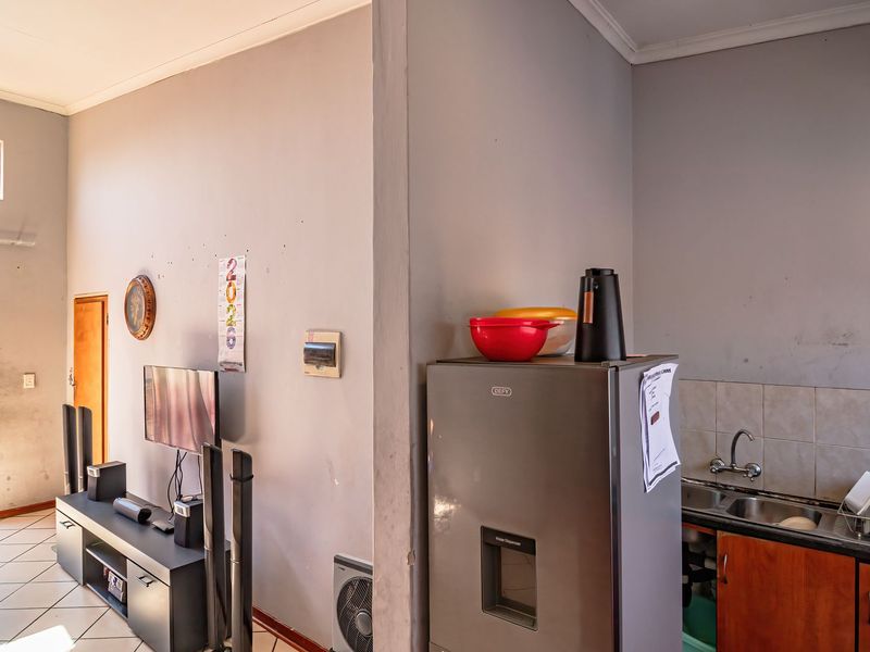 Open plan living area featuring tiled flooring, a compact kitchen with built-in cabinetry, and access to a balcony through a sliding door.