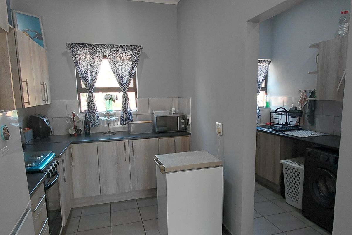 Functional kitchen featuring light wood-look cabinetry, dark countertops, and a tiled backsplash, with an adjoining scullery area for laundry and additional prep space.