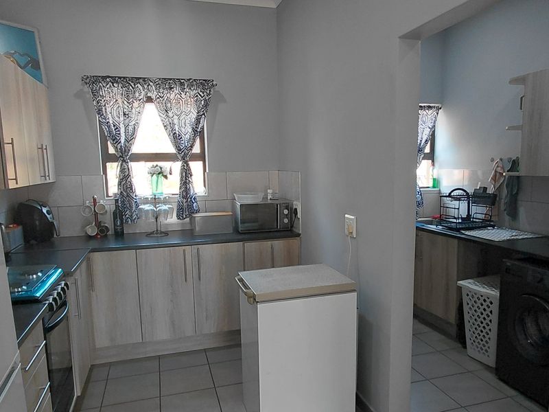 Functional kitchen featuring light wood-look cabinetry, dark countertops, and a tiled backsplash, with an adjoining scullery area for laundry and additional prep space.