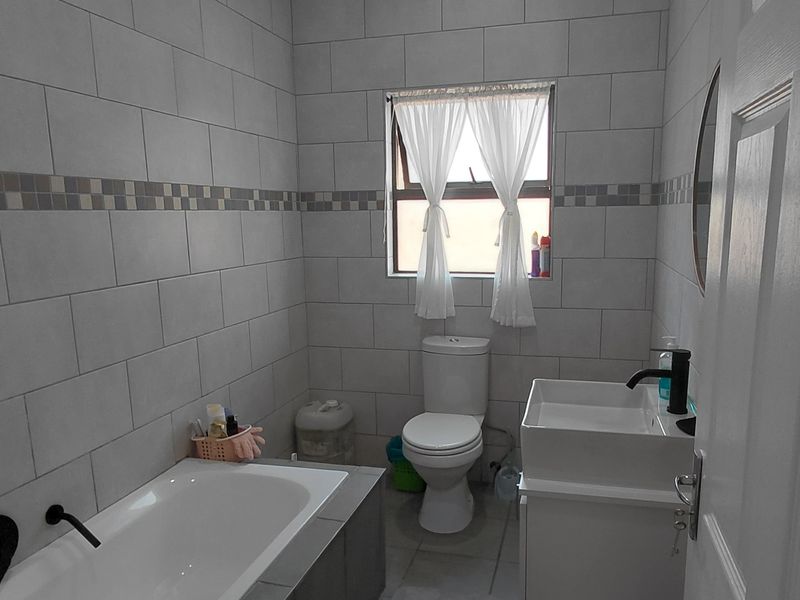 A modern bathroom featuring a bathtub, toilet, and vanity basin with contemporary tiled walls and flooring.