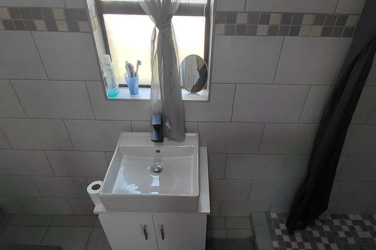 A compact bathroom featuring a modern vanity basin, tiled walls with a decorative mosaic border, and a shower area.