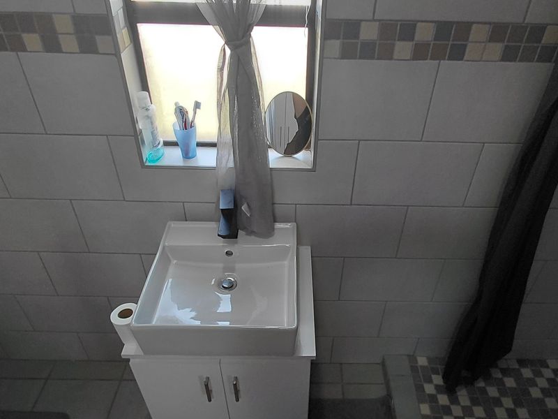 A compact bathroom featuring a modern vanity basin, tiled walls with a decorative mosaic border, and a shower area.