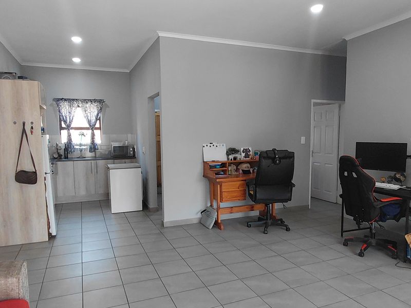 An open-plan living area featuring tiled flooring, recessed lighting, and a compact kitchen corner with built-in cabinetry and sink.