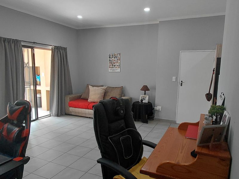 A spacious living area featuring neutral grey walls, tiled flooring, recessed lighting, and a sliding glass door providing access to an outdoor space.
