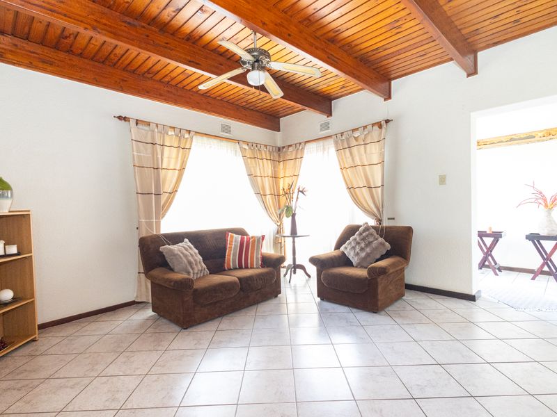 A living room featuring a vaulted timber-paneled ceiling with exposed beams, a ceiling fan, and neutral tiled flooring.