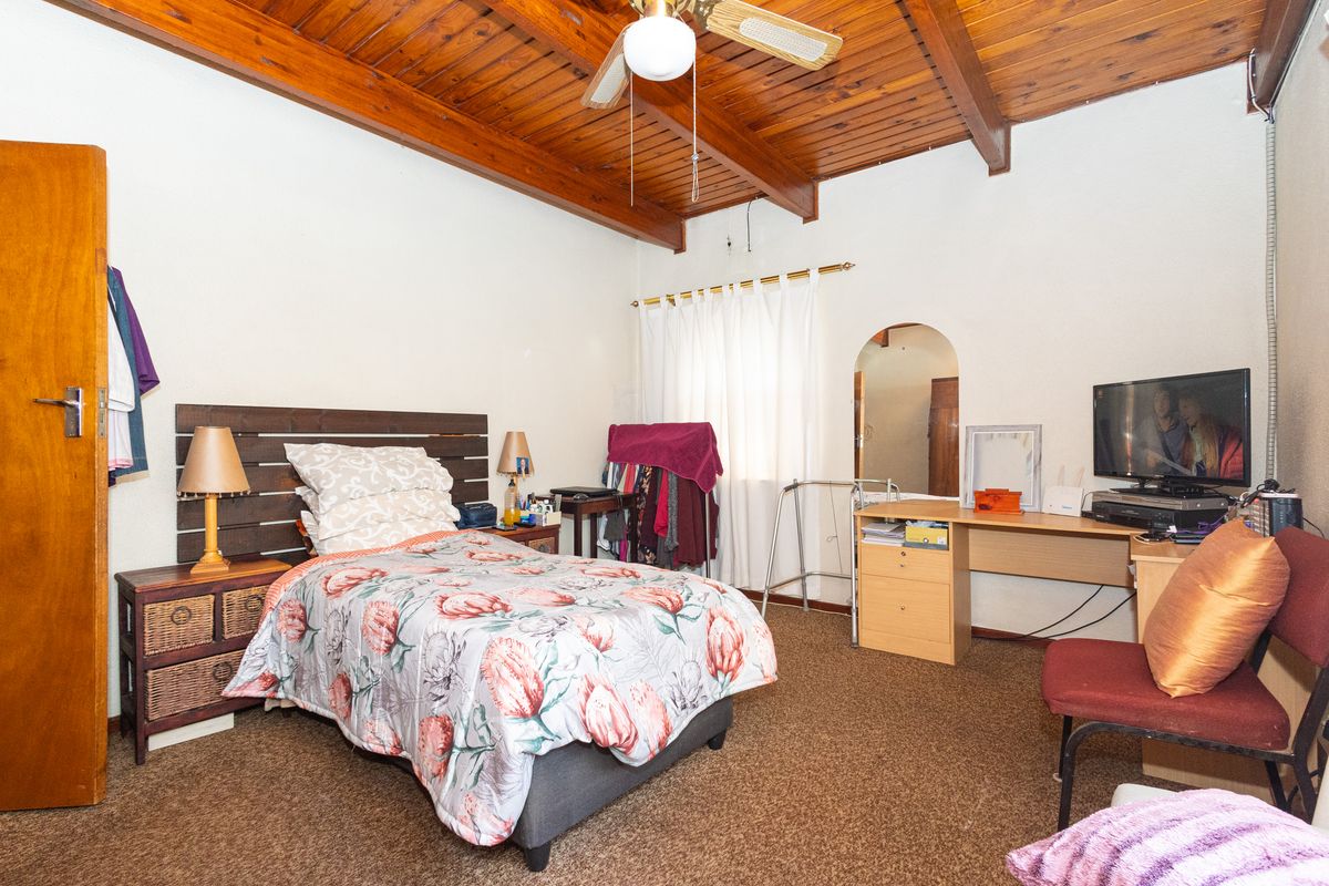 A bedroom featuring a vaulted timber beam ceiling, ceiling fan, and an arched doorway, providing a classic and functional living space.