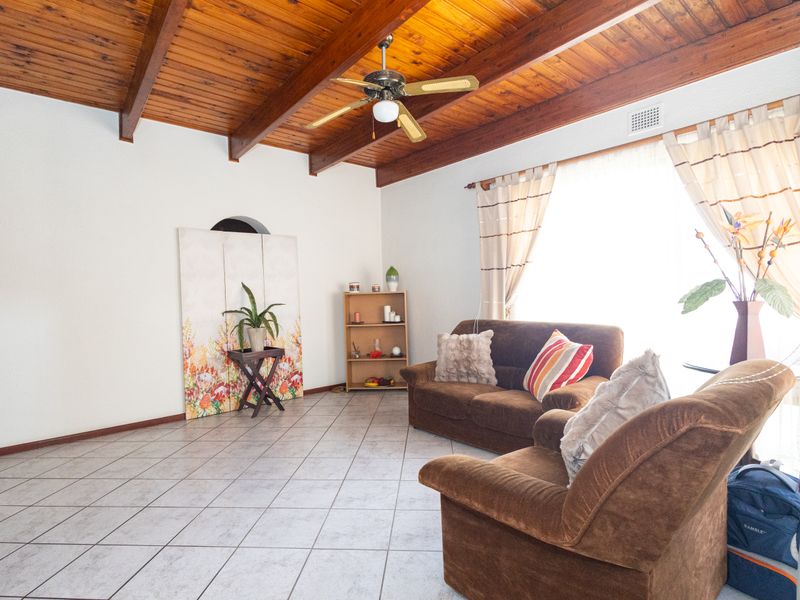 Spacious living room featuring a high exposed timber beam ceiling, ceiling fan, and neutral tiled flooring with ample natural light.