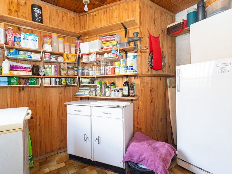 A functional scullery or pantry area featuring timber wall paneling, built-in cabinetry, and tiled flooring, providing ample storage space.