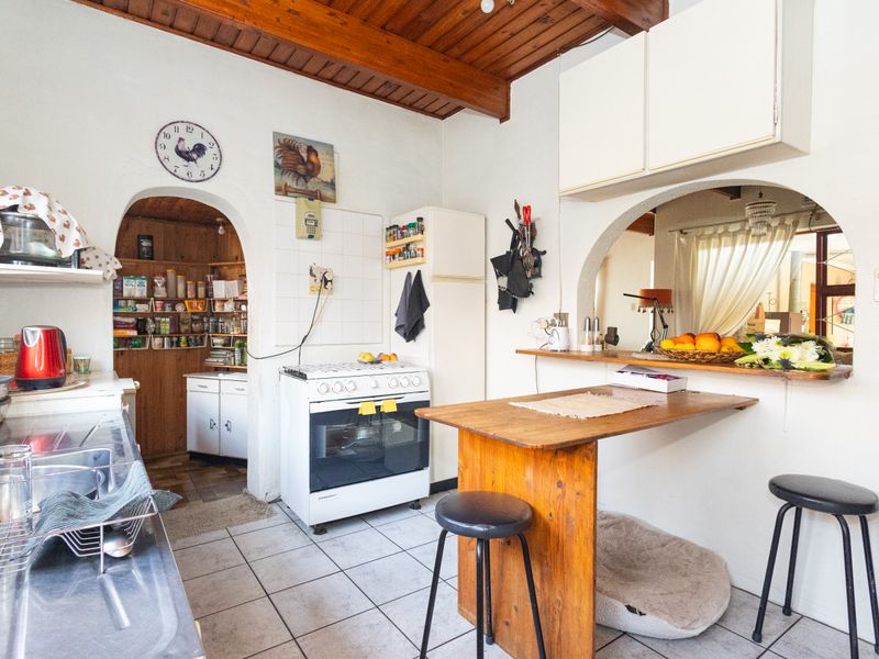 A dated kitchen featuring exposed timber ceiling beams, tiled flooring, a gas stove, and a breakfast bar with an adjacent arched pantry area.