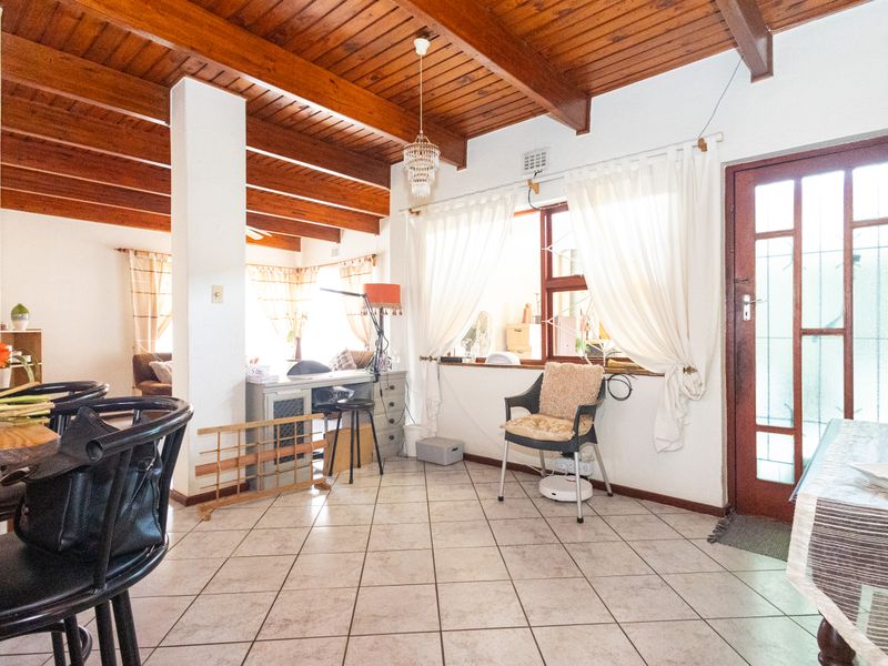 Open plan living area featuring exposed timber beam ceilings and tiled flooring, providing a warm and inviting space with direct access to the exterior.