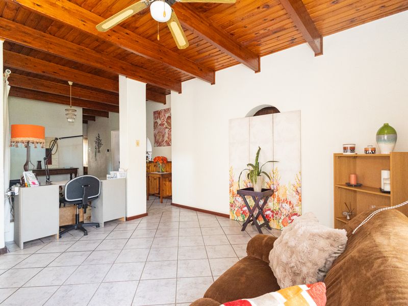 Spacious living area featuring a rustic exposed timber beam ceiling, ceramic tiled flooring, and a ceiling fan, offering a warm and inviting atmosphere.