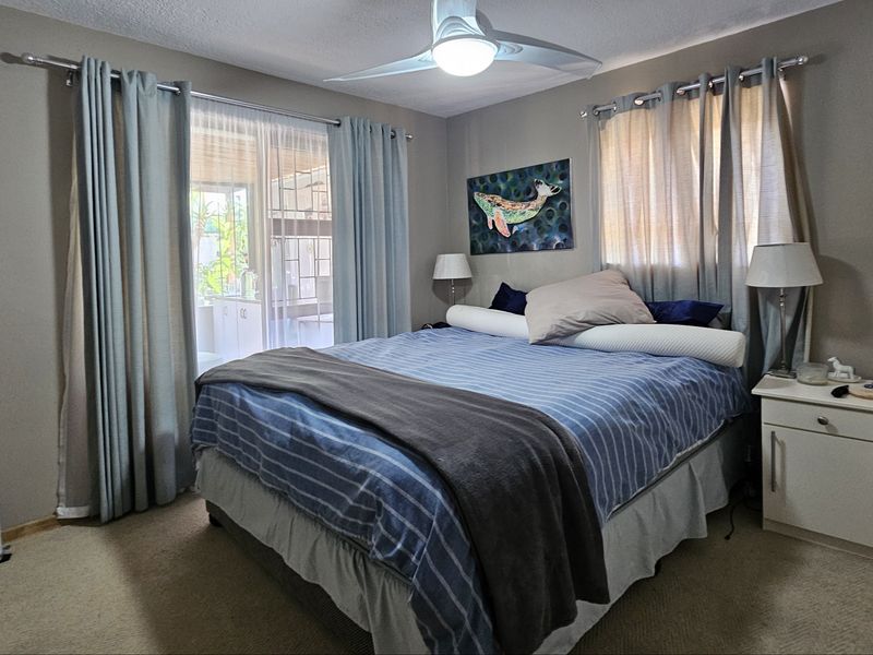 A comfortable bedroom featuring neutral wall tones, carpeted flooring, a ceiling fan, and a sliding glass door providing access to the outdoor area.