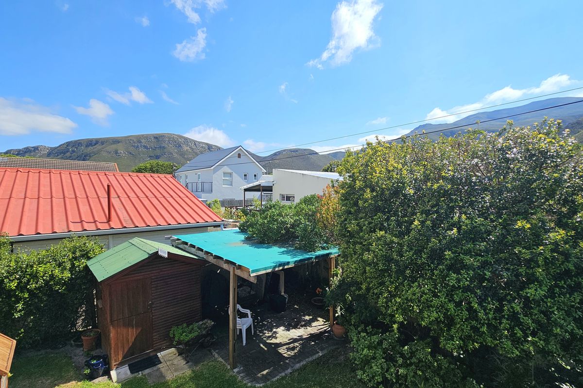 Rear exterior view showing a garden area with a timber shed, covered patio structure, and corrugated metal roofing against a mountain backdrop.