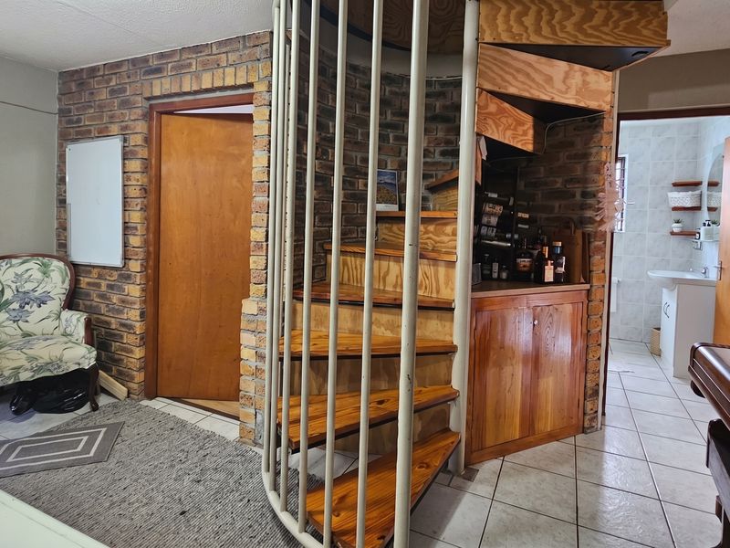 Living area featuring a prominent spiral staircase, exposed brickwork, and tiled flooring, with access to an adjacent bathroom.