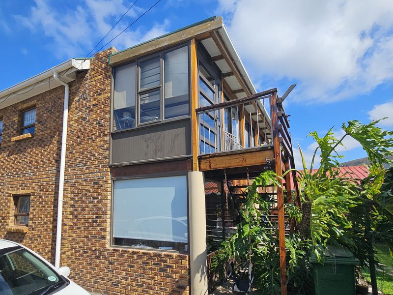 Rear view of the property featuring a brick facade, an elevated timber balcony, and an enclosed sunroom area with external staircase access.