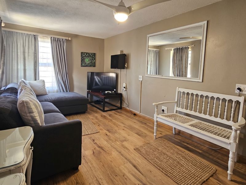 A living room featuring laminate flooring, a ceiling fan, and neutral wall tones, providing a functional and comfortable space for relaxation.