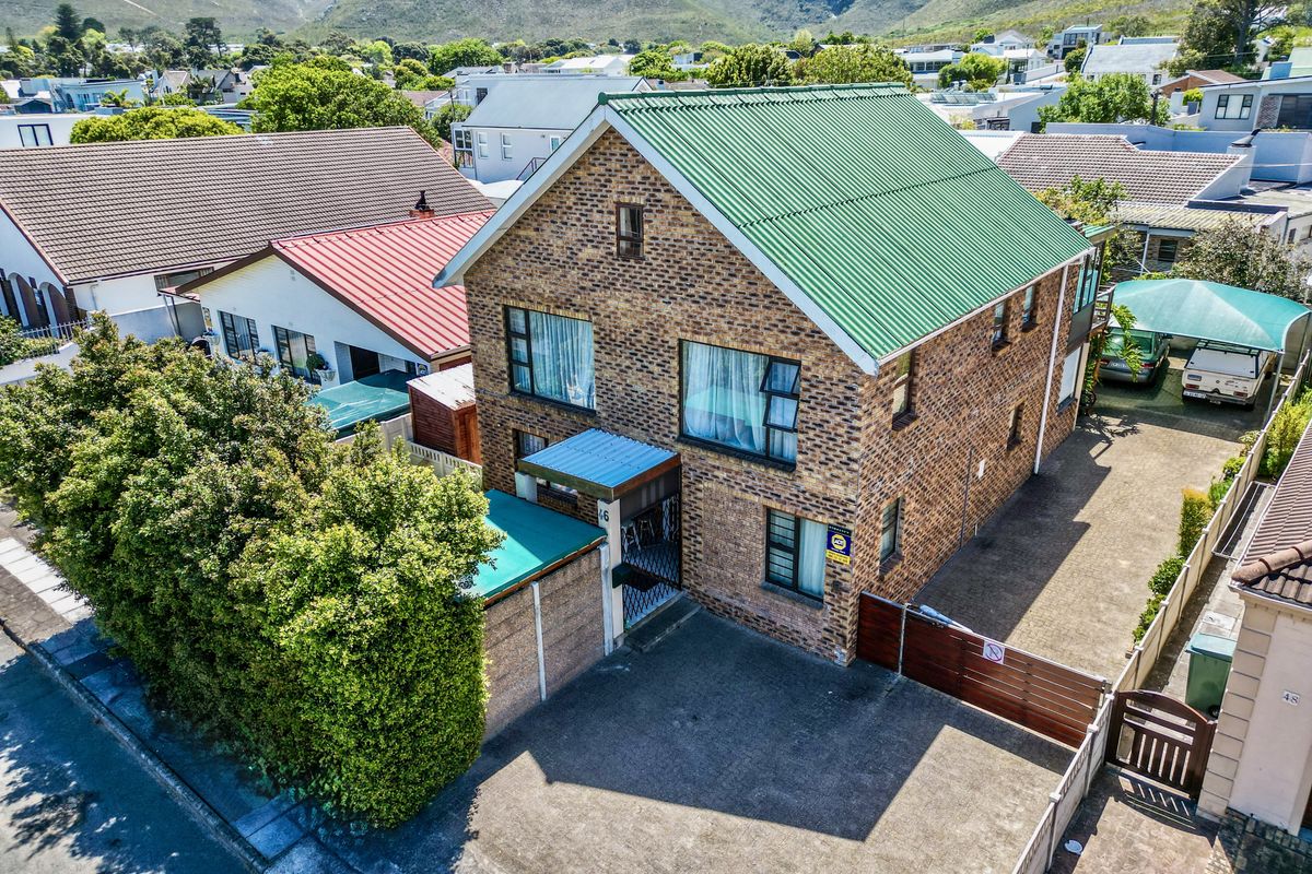 Aerial view of a double-story brick house featuring a green corrugated metal roof, paved driveway, and secure perimeter fencing in a residential neighborhood.