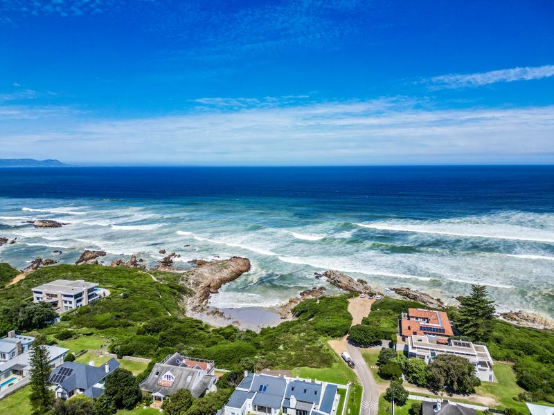 An aerial view of a coastal residential area featuring homes situated near the ocean and rocky shoreline.