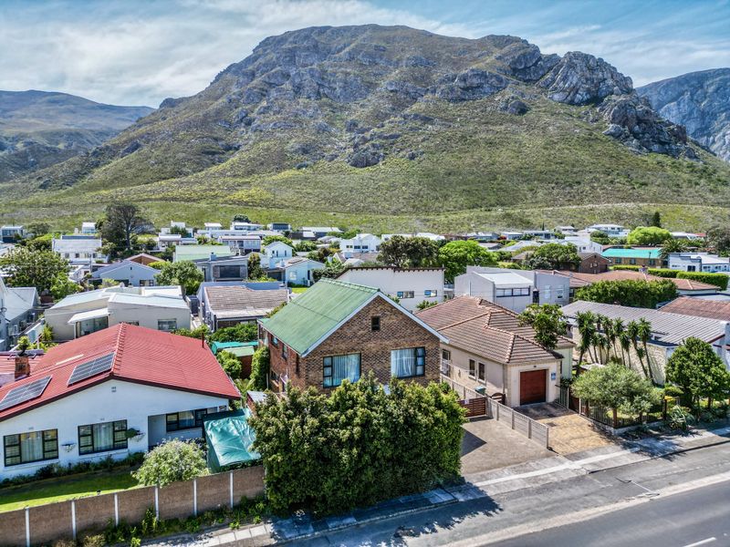 An aerial view of a residential property featuring a brick exterior, pitched roof, and driveway, set against a scenic mountain backdrop.