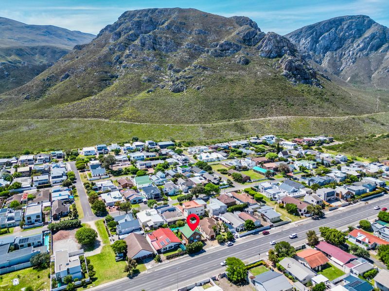 An aerial view of the residential property situated within a coastal neighborhood, featuring a prominent mountain backdrop and established street infrastructure.