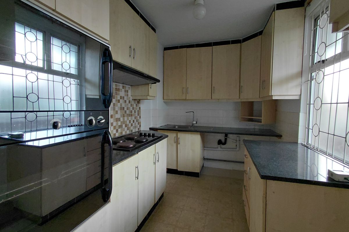 A functional kitchen featuring built-in oven, hob, extractor fan, laminate cabinetry, and dark countertops, requiring some cosmetic updates and repairs.