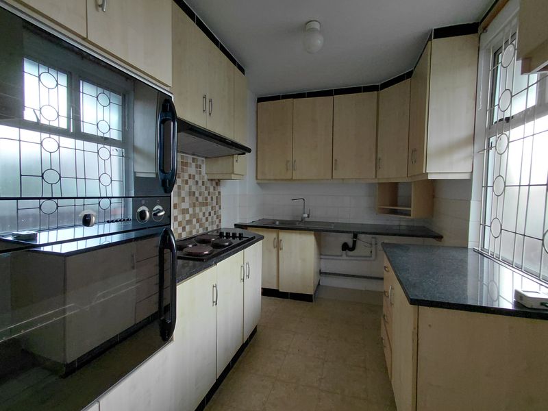 A functional kitchen featuring built-in oven, hob, extractor fan, laminate cabinetry, and dark countertops, requiring some cosmetic updates and repairs.
