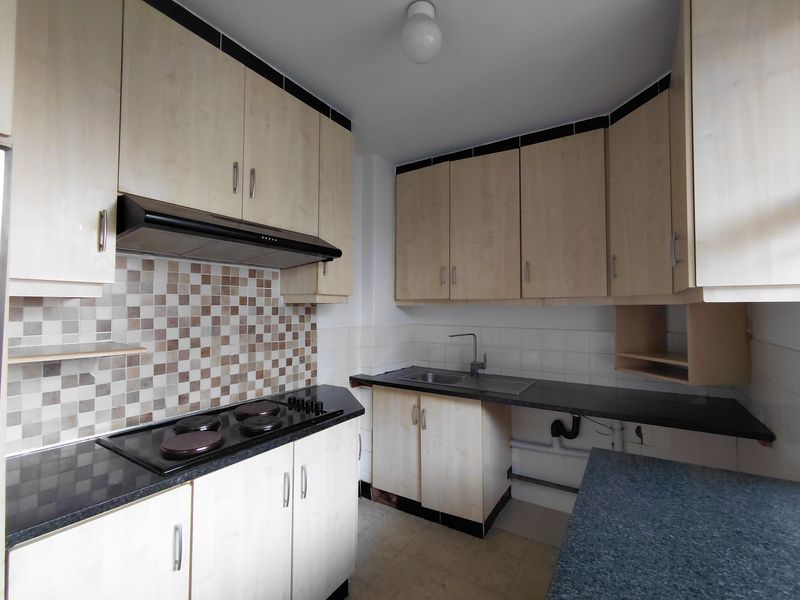 A functional kitchen featuring light wood-tone cabinetry, dark laminate countertops, a built-in electric hob with extractor fan, and a tiled backsplash.