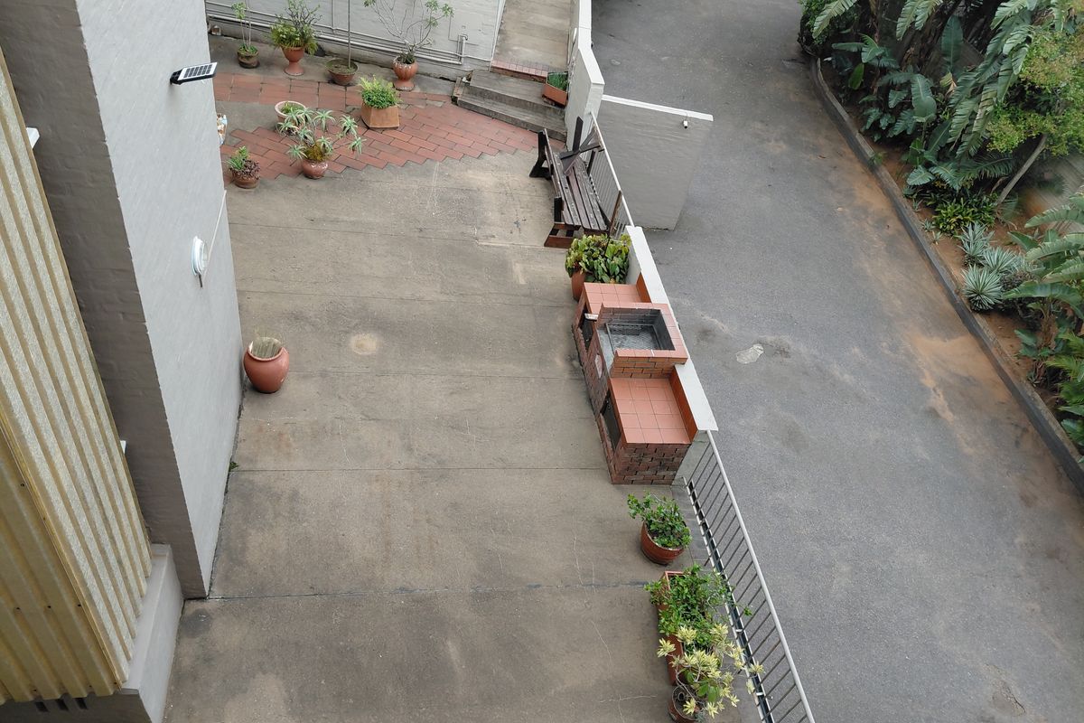 An elevated view of a rear concrete patio area featuring a built-in brick braai, paved sections, and perimeter metal railings.
