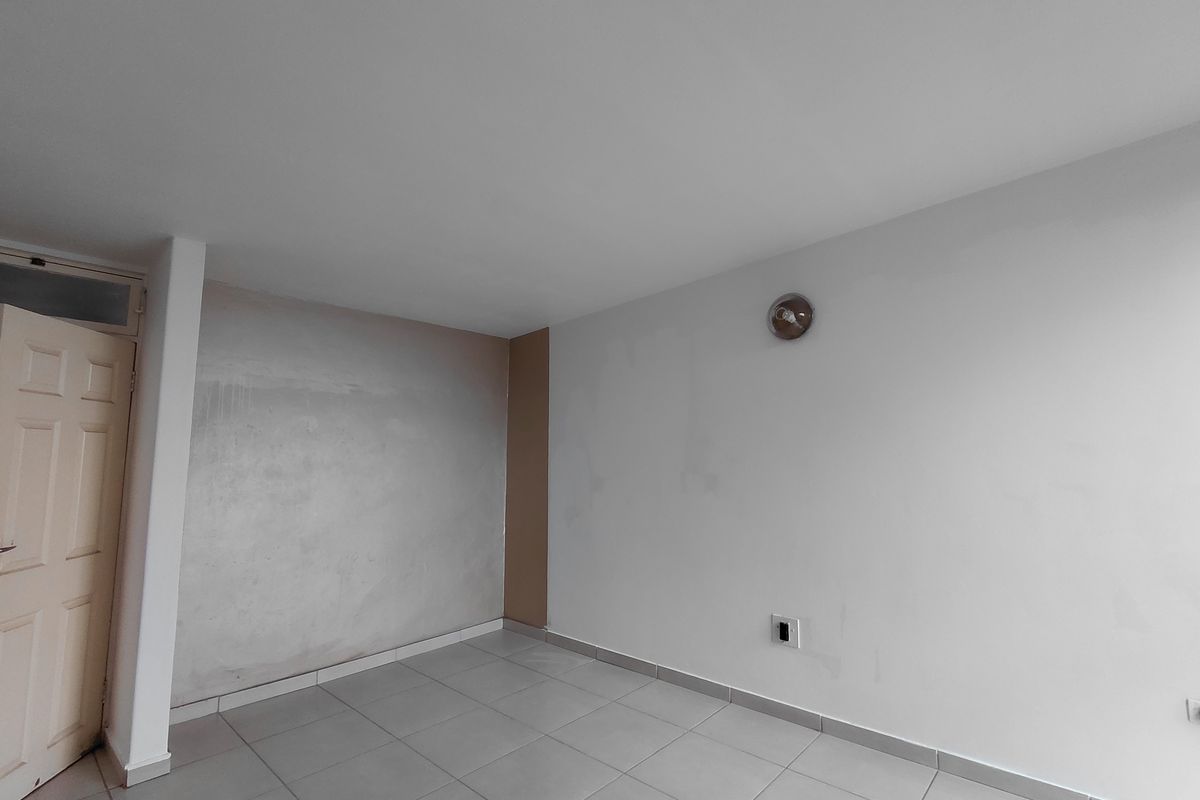An empty bedroom featuring tiled flooring, a wall-mounted light fixture, and a panel door, requiring cosmetic wall repairs and fresh paint.