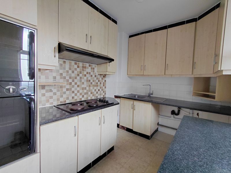 Functional kitchen featuring light wood-tone cabinetry, dark laminate countertops, built-in oven, electric hob, and a tiled backsplash.