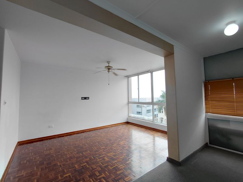 Spacious, empty living area featuring classic parquet flooring, a ceiling fan, and large windows providing ample natural light.